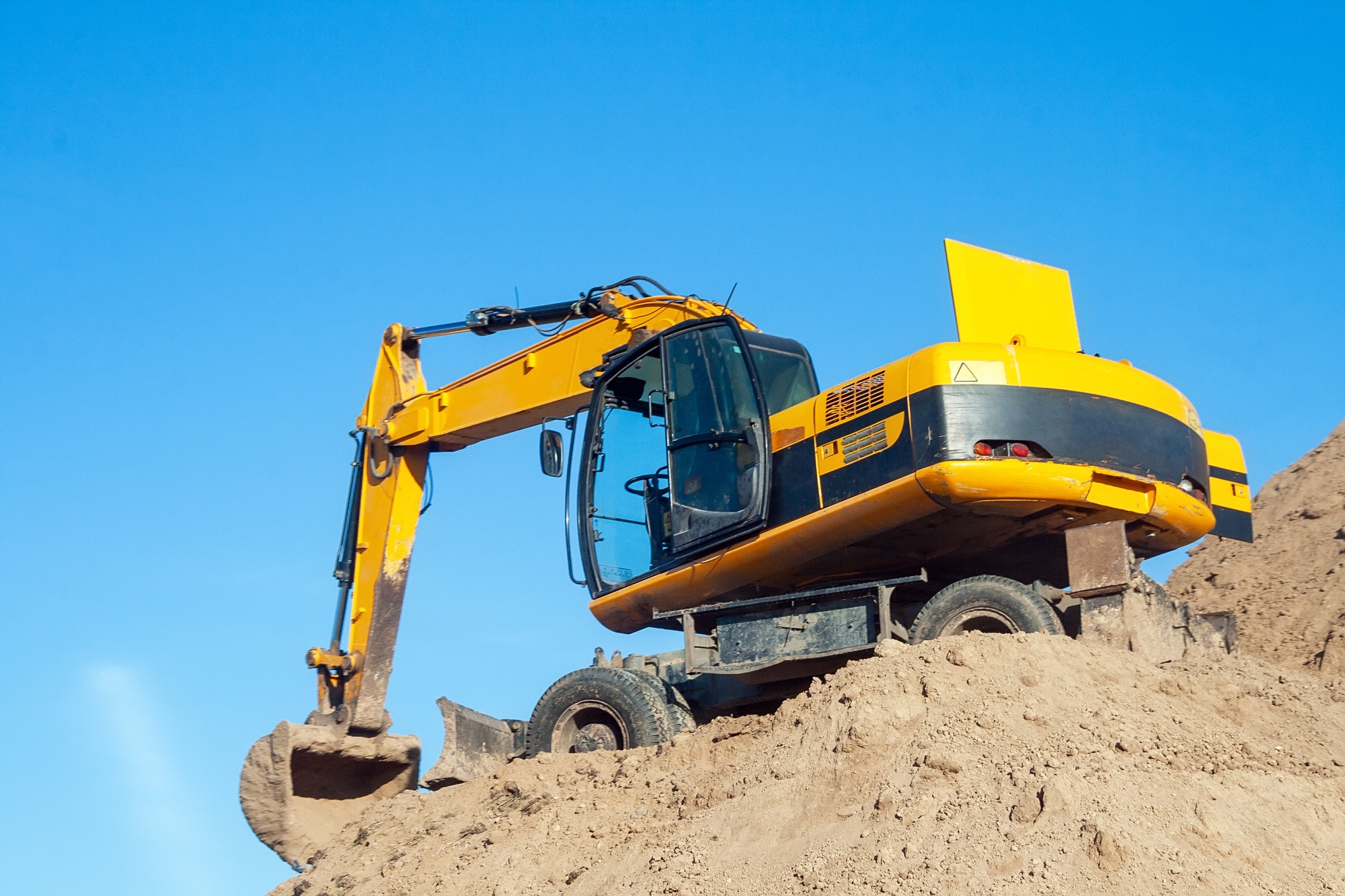 Excavator standing on large pile of ground against blue sky. Digger with bucket. Road work